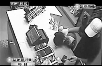 戴帽男子一手掐住加油站營(yíng)業(yè)員，一手持發(fā)令槍指向另一營(yíng)業(yè)員，要求“把錢(qián)給我裝起來(lái)”。