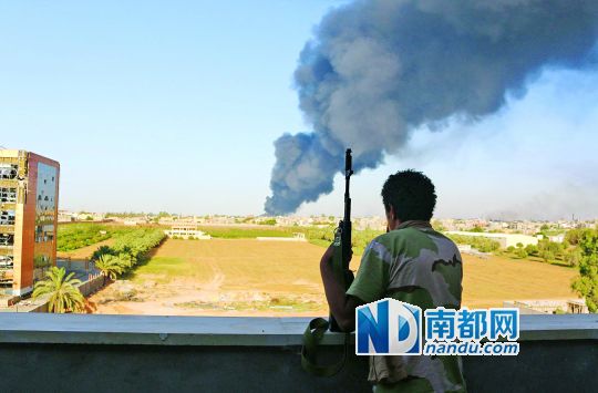 2日，利比亞首都的黎波里，一民兵武裝成員眺望被火箭彈擊中的儲油罐冒出濃煙。
