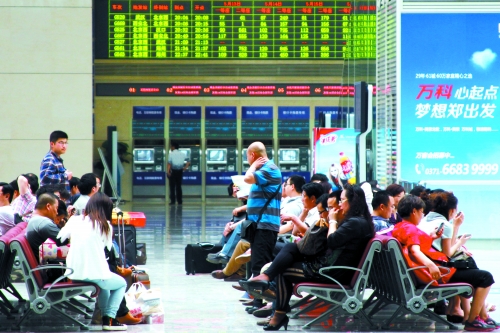 候車大廳溫度很高，一名乘客一手扇風(fēng)、一手擦汗