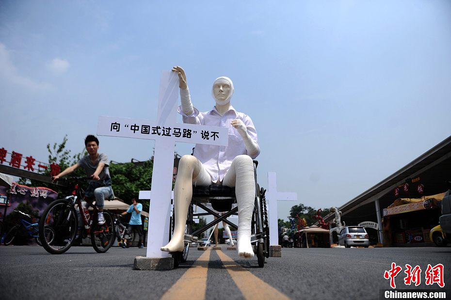 4月16日，重慶市洋人街上擺放著兩個(gè)受了傷的塑料人像“模特”，旁邊十字架上寫(xiě)著向“中國(guó)式過(guò)馬路”說(shuō)不