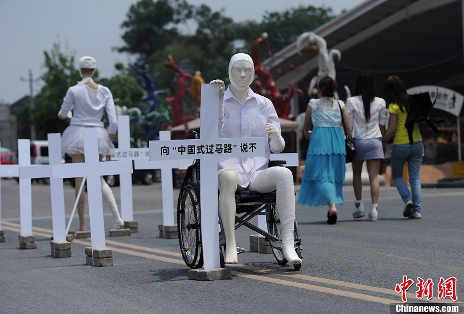4月16日，重慶市洋人街上擺放著兩個(gè)受了傷的塑料人像“模特”，旁邊十字架上寫(xiě)著向“中國(guó)式過(guò)馬路”說(shuō)不