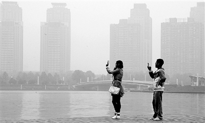 29日中午，鄭東新區(qū)如意湖畔，兩個(gè)年輕人拍攝霧霾中的景色。 鄭州晚報(bào)記者 馬健 圖