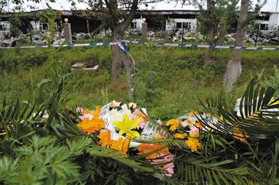 昨日，吉林省德惠市吉林寶源豐禽業(yè)有限公司燃燒事故現(xiàn)場警戒線外，遇難者家屬在路邊擺放了花圈祭奠逝去的親人。吳江 攝