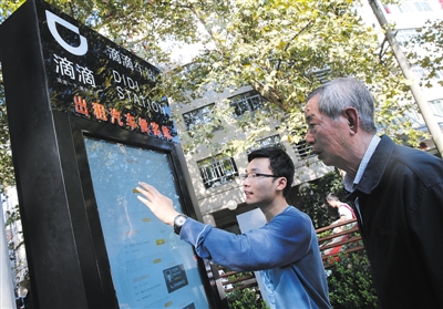 10月15日，滴滴工作人員（左）指導乘客使用“滴滴車站”的電子屏預約出租車。