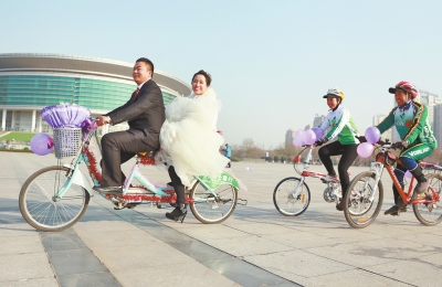 氣球和鮮花裝點(diǎn)的雙人自行車，新郎郝幸福載著美麗新娘回家。