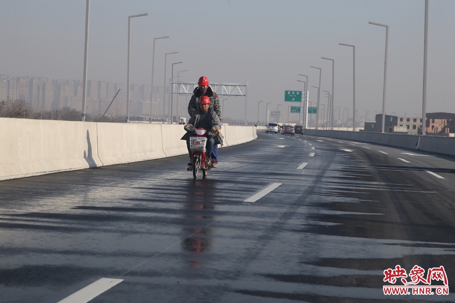 兩名工人騎車(chē)經(jīng)過(guò)灑水養(yǎng)護(hù)路面。
