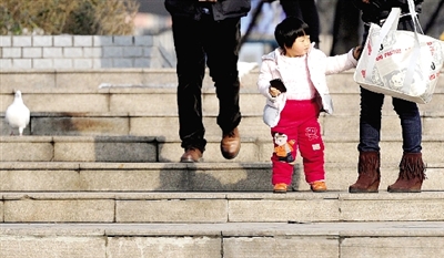 昨天中午，一女孩拉著家長(zhǎng)的手在紫荊山公園曬太陽(yáng)，氣溫升高，孩子的棉衣解開(kāi)了扣子。